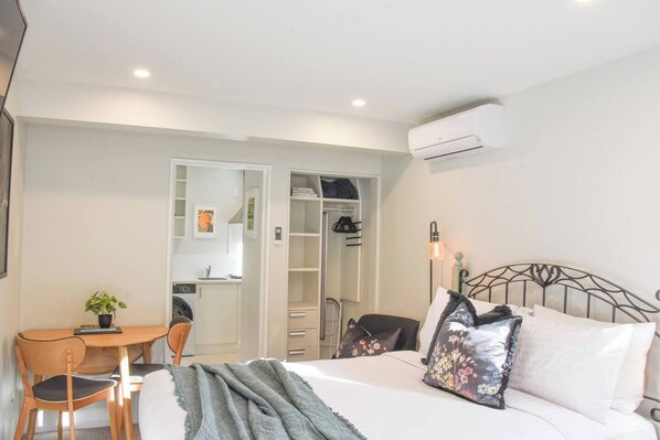 A bedroom with a bed, a desk, a chair, a wardrobe, and an air conditioning unit.