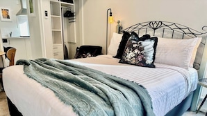 Uma cama com colchão branco e manta verde, cabeceira de metal preta e mesa de cabeceira com abajur.