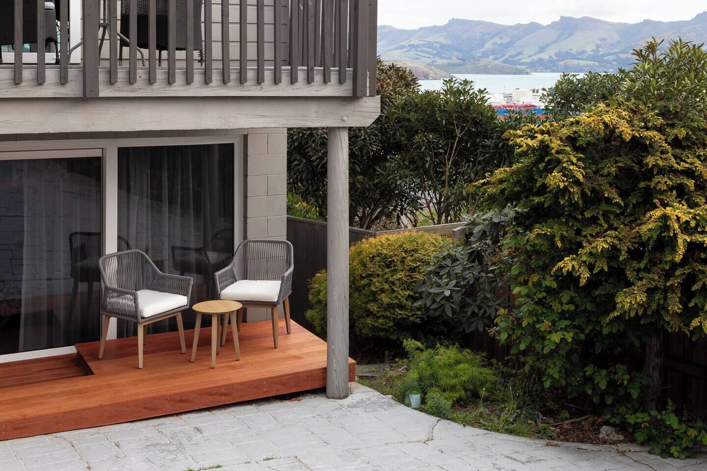 A modern outdoor seating area with two chairs and a small table, a wooden deck, and a view of a lake and mountains.