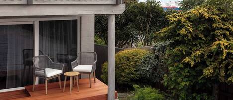 Un espacio exterior moderno con dos sillas y una mesa pequeña, una terraza de madera y vistas a un lago y montañas.