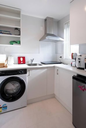 A compact kitchen with a built-in washing machine, a sink, and a window with blinds.