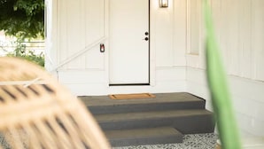 Un escalier menant à une porte dont le mur est texturé et au-dessus de laquelle est suspendu un luminaire.