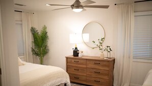 Une chambre à coucher avec un lit, une commode en bois, un miroir et un ventilateur de plafond.