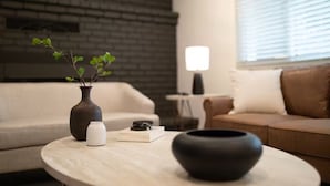 Un salon avec un canapé, une table basse ornée d’un vase et de livres, et une lampe.