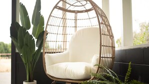 Une chaise en osier avec un coussin, une plante en pot et un sol à motifs.