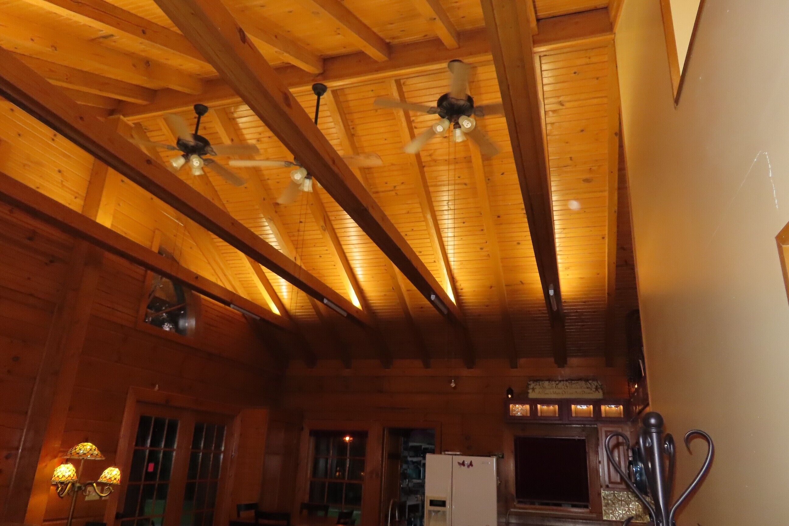 A wooden interior with exposed beams, a ceiling fan, and a refrigerator.