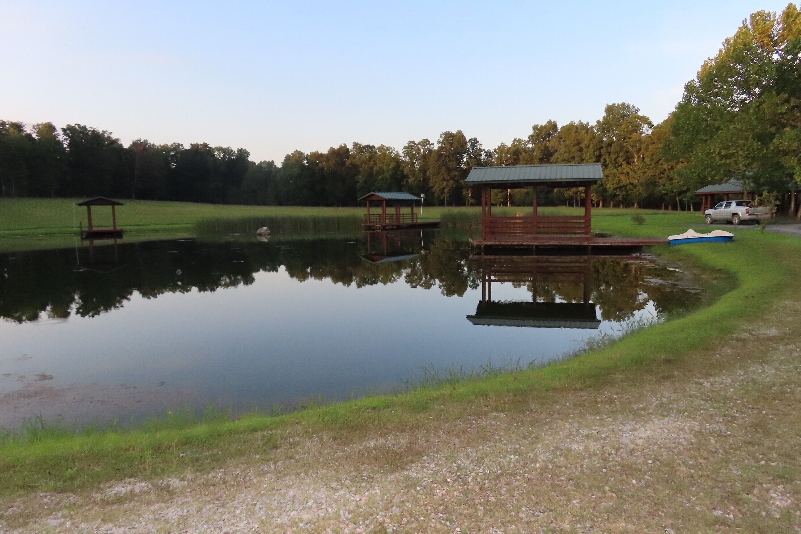 A tranquil lake with wooden docks and a gazebo, surrounded by trees and a grassy area.