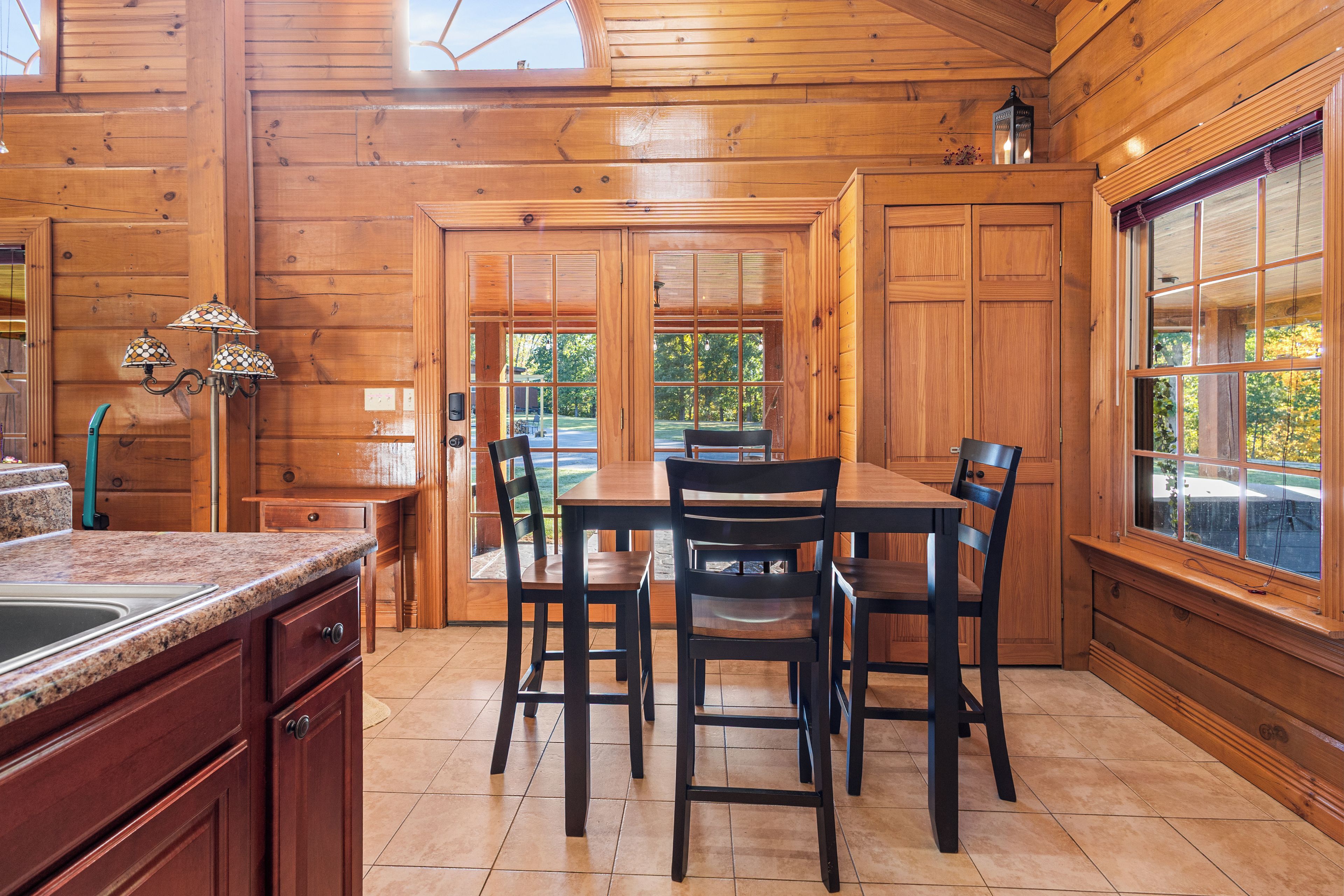 A wooden interior with a dining table and chairs, a kitchen area with granite countertops, and large windows.
