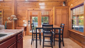 A wooden interior with a dining table and chairs, a kitchen area with granite countertops, and large windows.