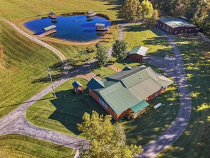 An aerial view of a property with a large building, a pond with docks, and a well-maintained lawn.