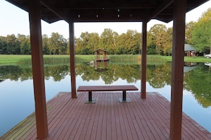 A wooden deck with a bench and a gazebo over a calm lake, surrounded by trees.