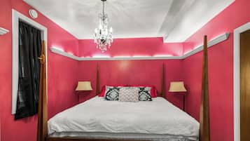 A bedroom with a four-poster bed, two bedside lamps, a chandelier, and a window with curtains.