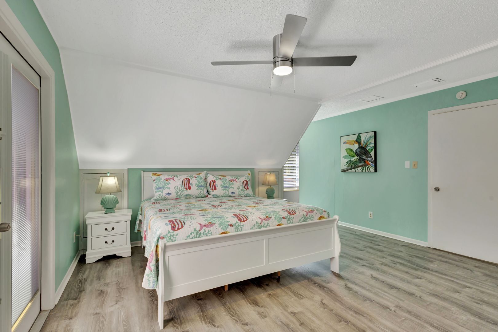 Camera da letto con un letto, comodini, una ventola a soffitto e un'opera d'arte appesa al muro.