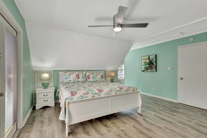 A bedroom with a bed, bedside tables, a ceiling fan, and a wall-mounted artwork. - Jensen Beach Tropical Resort (Fort Pierce)