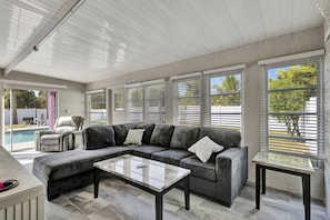 A modern living room with a sectional sofa, a coffee table, and a pool view. - Jensen Beach Tropical Resort (Fort Pierce)