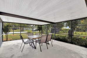 A covered patio with a table and chairs, large windows, and a view of a landscaped garden. - Jensen Beach Tropical Resort (Fort Pierce)