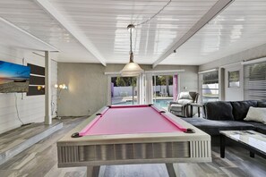 A pool table in a room with a ceiling fan, a sofa, and a television on the wall.