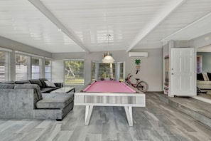 A modern living room with a pool table, a gray sofa, and a bicycle. - Jensen Beach Tropical Resort (Fort Pierce)