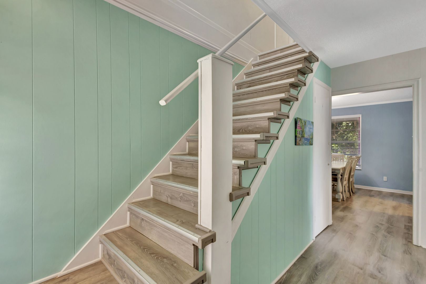 A staircase with wooden steps and white railings, leading to a dining area with a table and chairs.