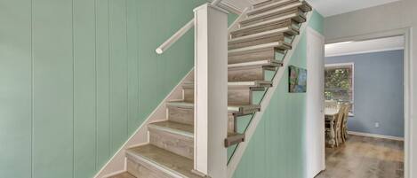 A staircase with wooden steps and white railings, leading to a dining area with a table and chairs.