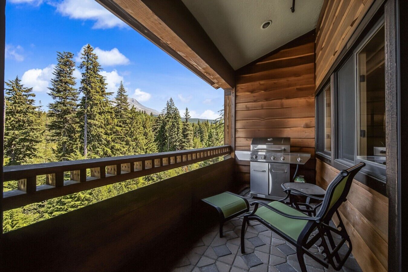 A balcony with a grill, chairs, and a view of a forest.