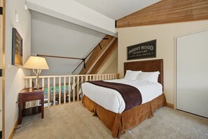 Ein Schlafzimmer mit einem Bett, einem Nachttisch, einer Lampe, einer Treppe und einem Schild mit der Aufschrift 'Mount Hood Adventure'.