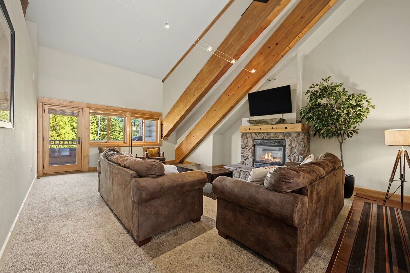 A spacious living room with a stone fireplace, a large flat-screen TV, and a cozy seating area with two sofas.