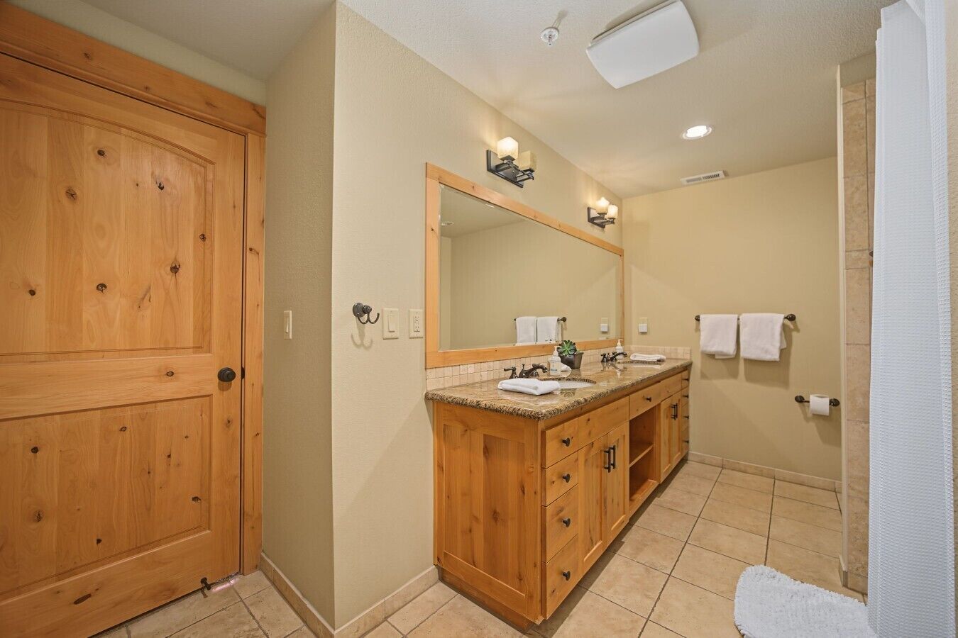 Un baño con armarios de madera, un espejo grande y dos lavamanos.