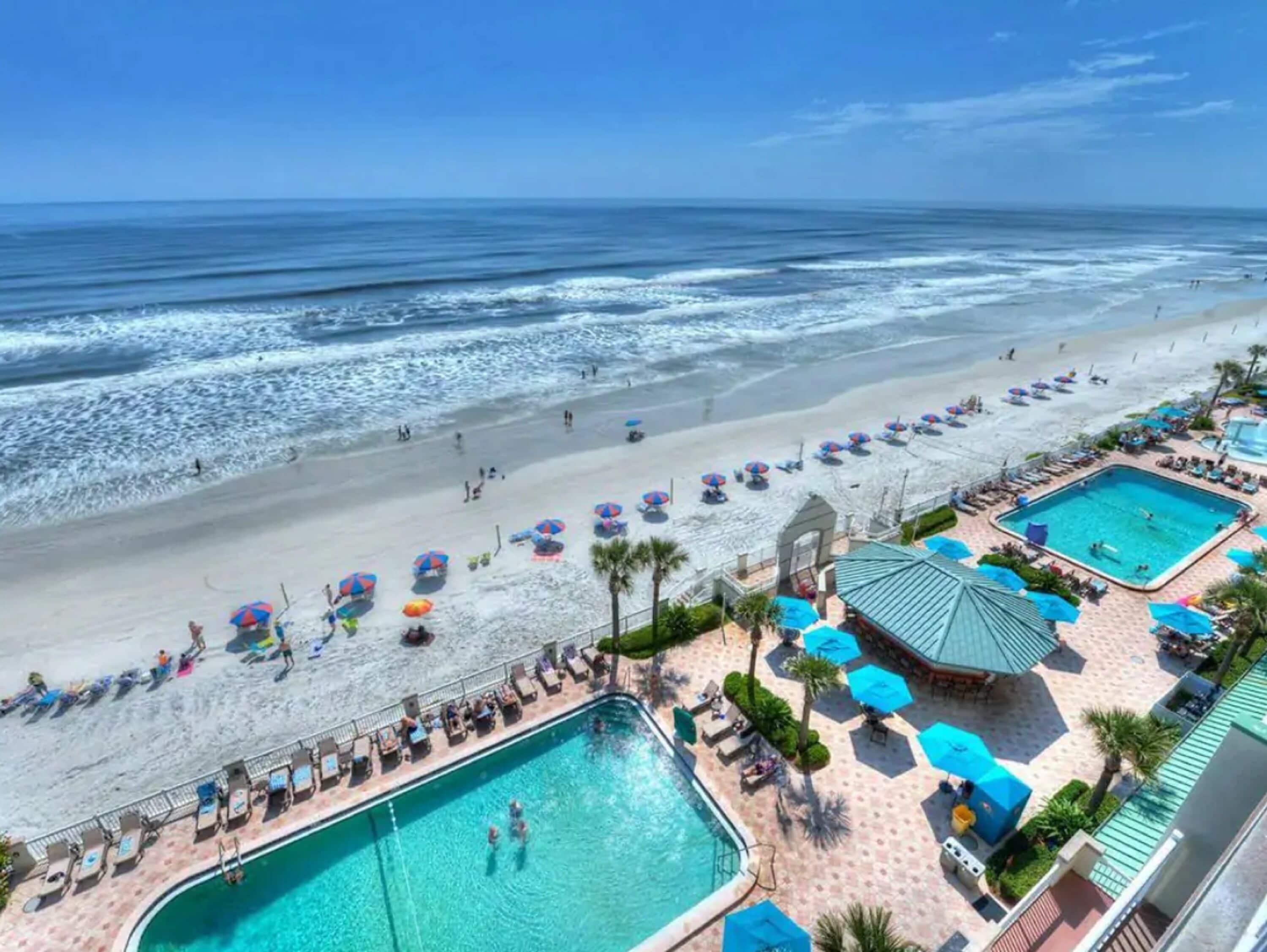 A beach resort with a swimming pool, beach umbrellas, and a view of the ocean.
