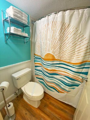 Une salle de bain comprenant des toilettes, un rouleau de papier toilette, un porte-serviettes avec des serviettes pliées et un rideau de douche orné d'un motif solaire.