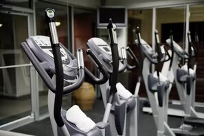 Une rangée de vélos d’appartement dans une salle de sport, avec un mur de verre en arrière-plan.