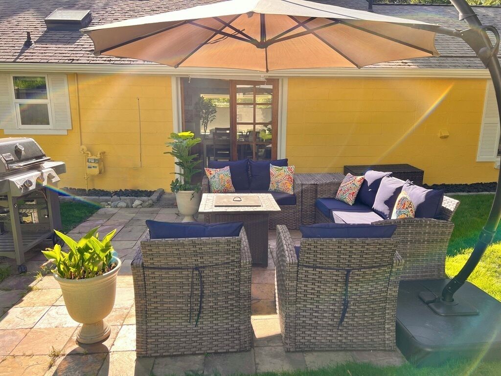 Een terras buiten met rieten meubels, een barbecue en een grote parasol.