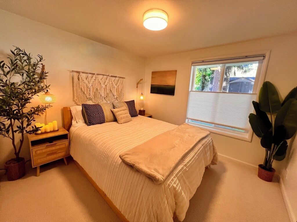 Een slaapkamer met een bed, nachtkastje, lamp en een raam met zonwering.