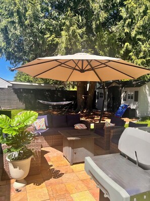 Eine Terrasse im Freien mit einem großen Sonnenschirm, Korbmöbeln und einer Hängematte.
