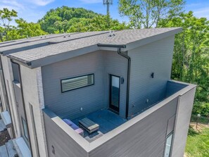 A modern two-story building with a flat roof, a balcony, and a small outdoor seating area.