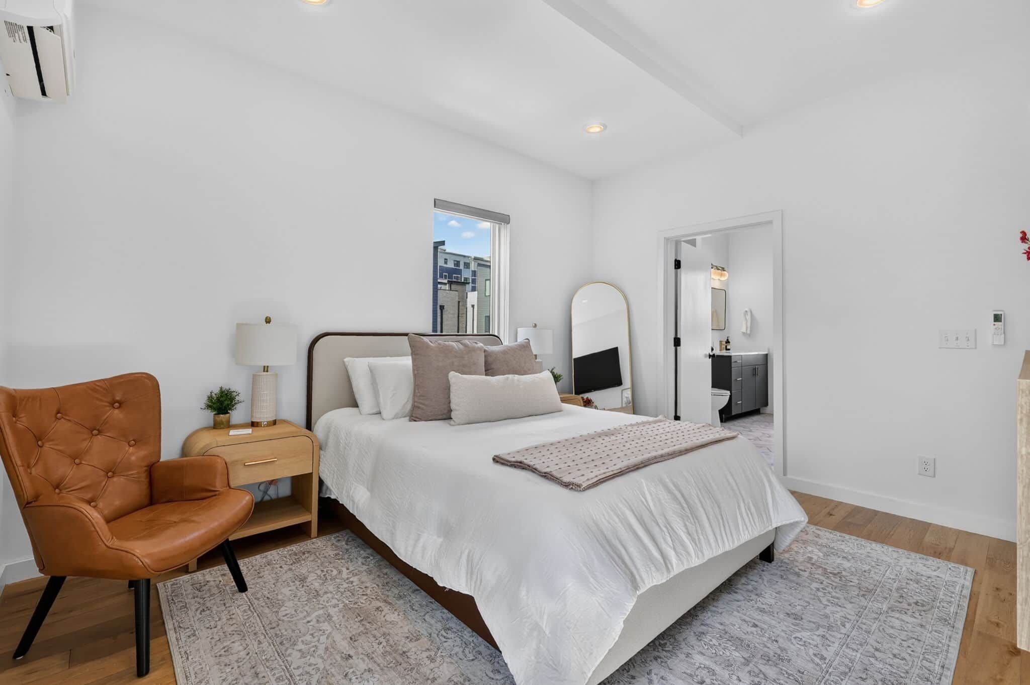 A bedroom with a bed, a chair, a nightstand, a mirror, and a window.