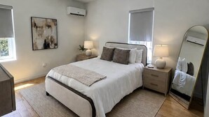 Une chambre à coucher moderne avec un grand lit, des tables de chevet, un miroir et des œuvres d’art accrochées au mur.