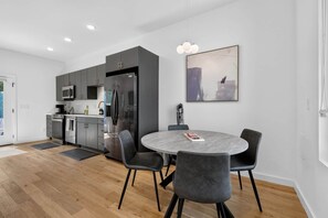 A modern kitchen with grey cabinets, a stainless steel refrigerator, and a dining area with a round table and four chairs.