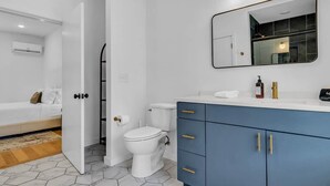 Une salle de bain moderne avec des toilettes, un lavabo surmonté d’un miroir et un meuble bleu avec des poignées dorées.