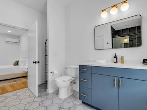 A modern bathroom with a toilet, a sink with a mirror above, and a blue cabinet with gold handles. - The Saint Luxury Townhome: steps to UTK/Downtown (Knoxville)