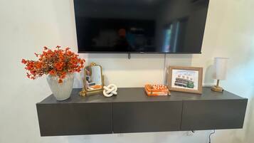 A flat-screen TV mounted on a dark wall above a black console with a vase of flowers, a framed picture, and a small lamp.