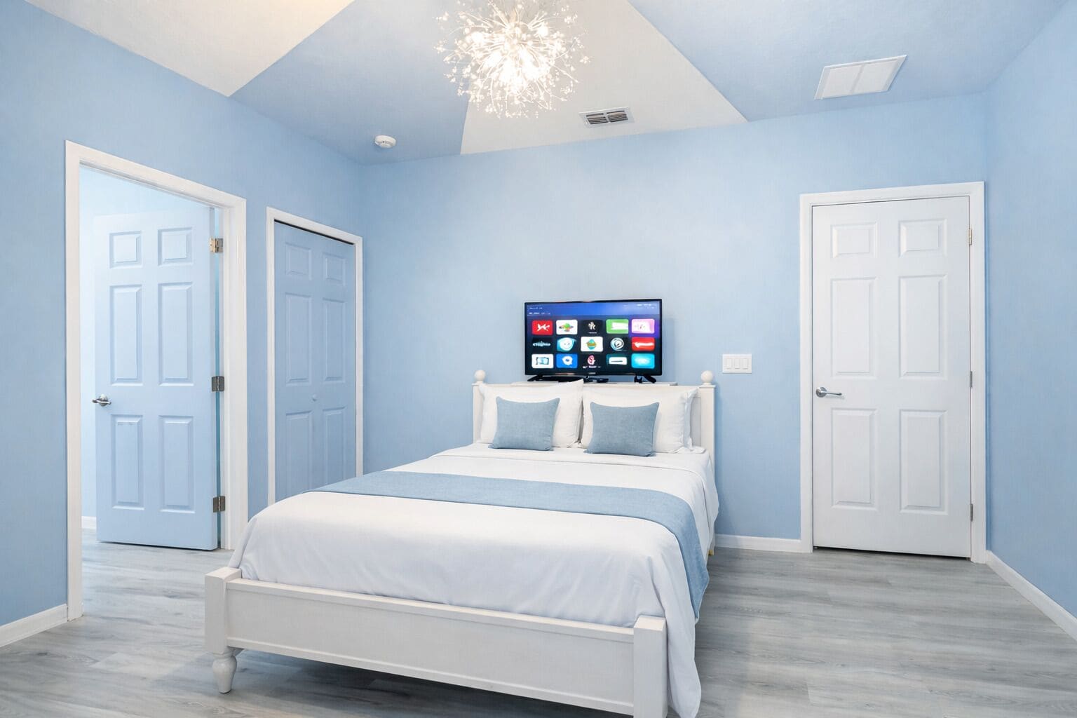 A bedroom with a bed, a TV mounted on the wall, and two doors.