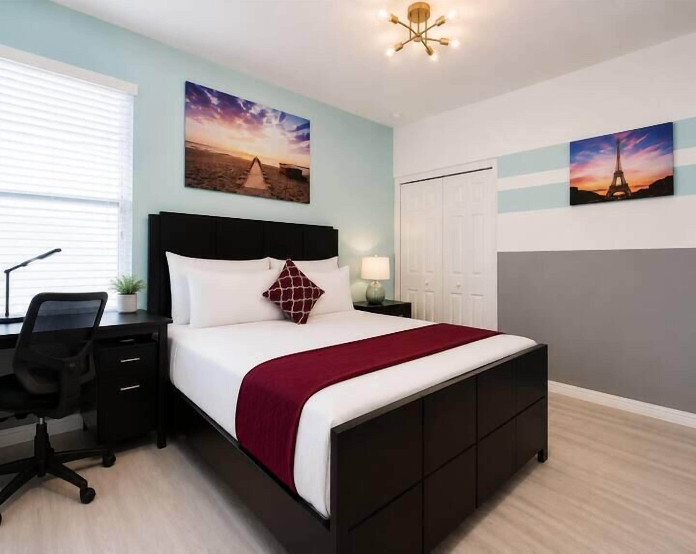 Een slaapkamer met een bed, bureau, stoel en kunstwerken aan de wanden.