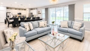A modern living room with a grey sofa set, a glass coffee table, and a dining area in the background.