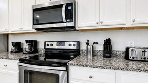 A kitchen with white cabinets, a stainless steel microwave, a stove, a coffee maker, a toaster, and a utensil holder.