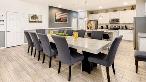 Une cuisine moderne avec des meubles blancs, un îlot central et un coin repas comprenant une table en marbre et des chaises grises.