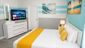 A hotel room with a bed, a TV on a dresser, a door, and a wall with a painting.