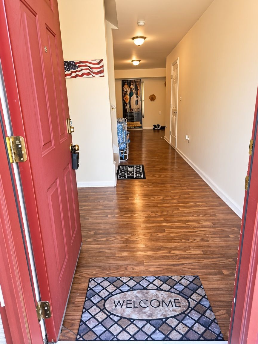 A hallway with a red door, a welcome mat, and a poster on the wall.
