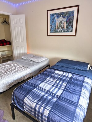 A bedroom with two beds, a wardrobe, and a framed picture on the wall.