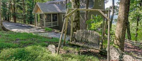 A wooden cabin with a porch, surrounded by dense forest.